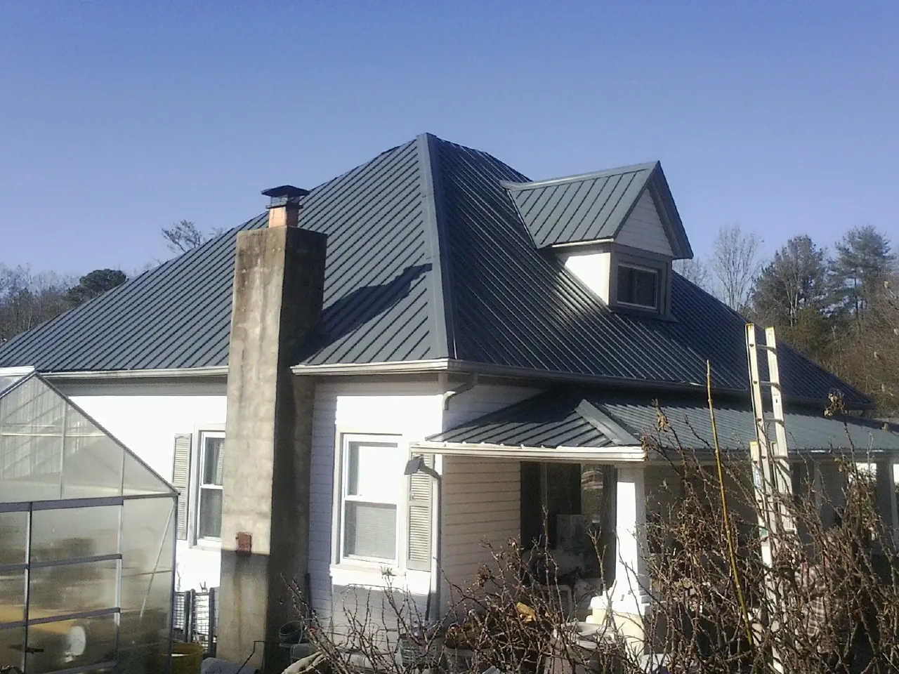 Dark blue standing seam metal roof on a white farmhouse with dormer — Slate & Tile Roof Repair by Roofing Brothers in Mountainside