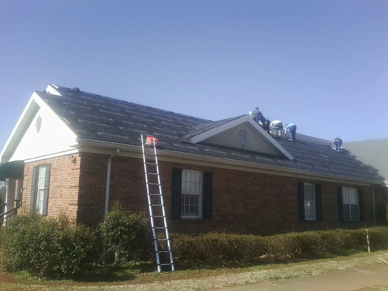 Crew tearing shingles off a brick ranch roof with a ladder set — Emergency Roof Repair work by our crew in Mountainside