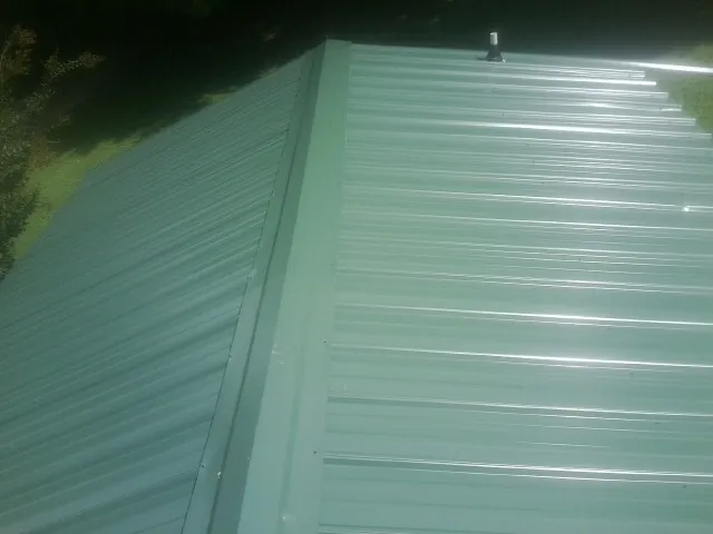 New green metal panels meeting at the ridge of a roof — Flat Roof Repair work by our crew in Mountainside
