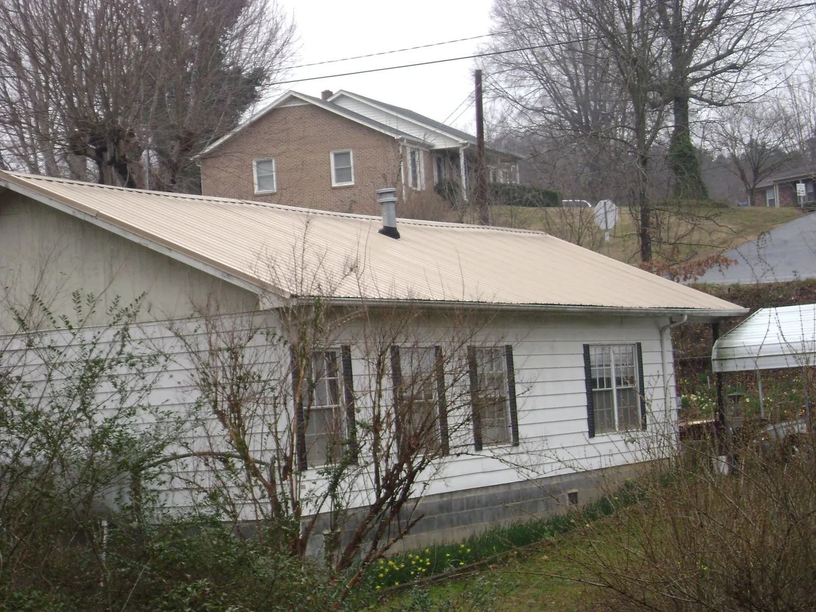 Tan metal roof on a white sided house set into a hillside — Commercial Roofing by Roofing Brothers in Mountainside